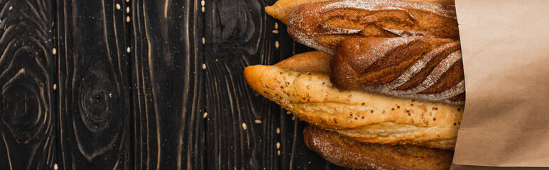 top view of fresh baked baguette loaves in paper bag on wooden black surface, panoramic shot