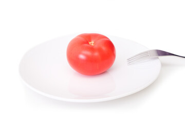 One single red ripe fresh raw tomato on white ceramic plate with a folk isolated on white, mediterranean diet concept