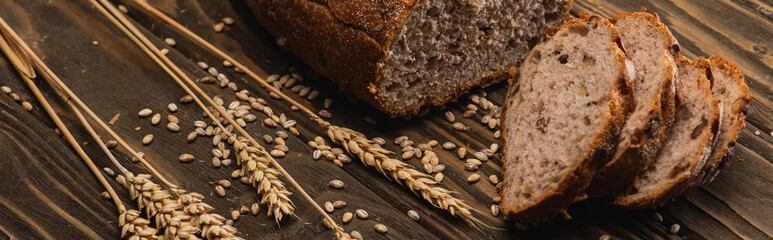 cut fresh baked bread with spikelets on wooden surface, panoramic shot