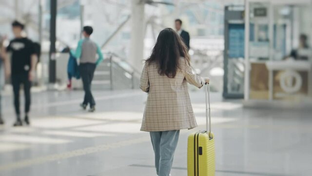 Silhouette of young woman heading to escalator to platform. Girl going with suitcase to aboard train in light beautiful station. Woman preparing for business trip or vacation. Concept of travel.