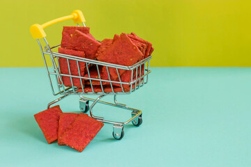 Natural beetroot crackers or biscuits in a shopping basket on a double yellow and blue background. Healthy food concept for wellness. Diet products. Copy space.