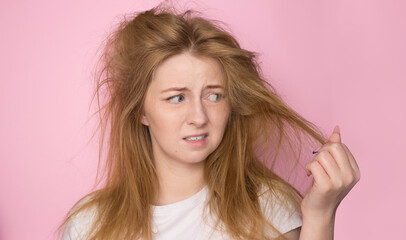 The concept of dry lifeless hair. A woman on a pink background holds her disheveled, tangled hair...