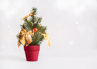 Toy Christmas tree Poster template with copy space New year decoration Small pine tree with gold bows in red pot on white background with blurred lights around