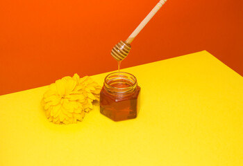 Bee honey drips from a wooden spatula into a glass jar. Flower, yellow-red background. Useful farm products.