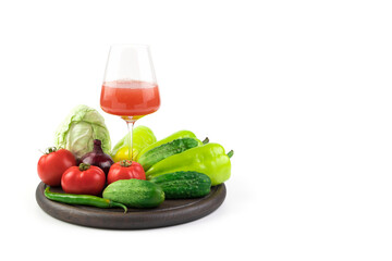 A glass of freshly squeezed vegetable juice and fresh vegetables on a round tray on a white background. Vegetable background. The concept of proper nutrition.