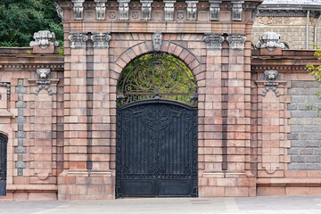 Brick wall with portal and old closed black iron gate