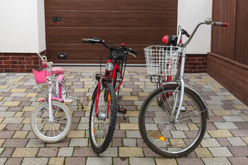 Three family bikes stand in the yard against the backdrop of the garage door