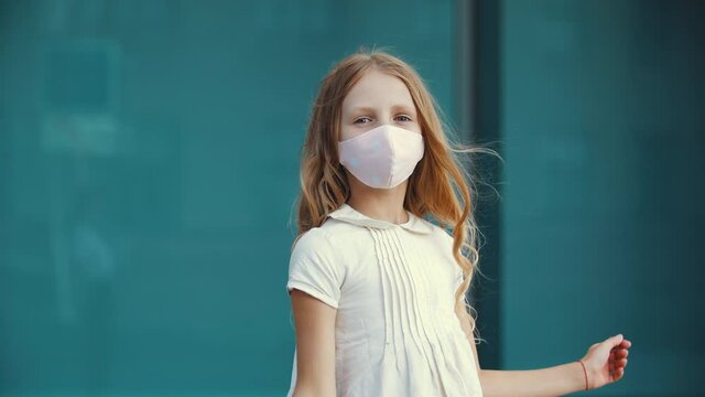 Little girl wears protective medical mask from virus, shows thumb up to camera, sign of consent, like concept, symbol of satisfaction, rejoices in freedom, school canceled due to quarantine pandemic