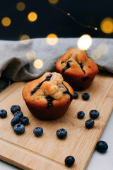 Blueberry muffins on wooden board with some fresh blueberries and bokeh on the background. Cozy food background.