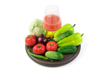 A large selection of vegetables and a Glass of freshly squeezed vegetable juice on a round tray on a white background. Vegetable background. The concept of proper nutrition.