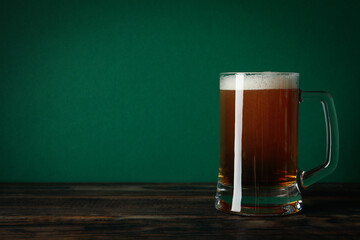 Glass of beer on wooden table against green background