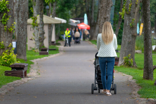 Blonde hair young mother with baby in a stroller walking in a park by a lake - Powered by Adobe