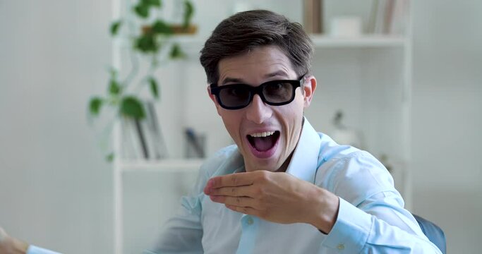 Head shot of young eccentric enthusiastic man, funny guy wears black glasses, shows like sign of approval, sign of consent, rips off his thumb, demonstrates magical comic trick, actively moves hands