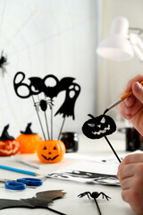 Preparing for Halloween. DIY concept. Crop Male hands painting paper pumpkin black, halloween decoration on white desk, indoor. Daytime. Copy space, vertical orientation.