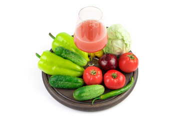 A glass of freshly squeezed vegetable juice and fresh vegetables on a round tray on a white background. Vegetable background. The concept of proper nutrition.