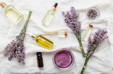 Fototapeta na wymiar Set lavender oils serum and lavender flowers on white fabric. Skincare cosmetics products. Natural spa beauty products. Lavender essential oil, serum, body butter, massage oil, liquid. Flat lay
