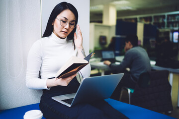 Asian woman reading book and using laptop