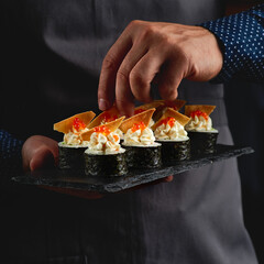 Sushi roll maki futo japanese food on a black stone plate in the hands of a waiter. Close up