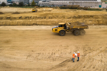 Obraz premium Top view of two road construction workers in orange vests and protective helmets in the middle on the field