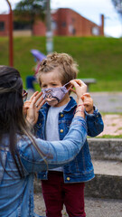 Caucasian mother putting face mask on her son in the park, Back to School
