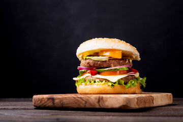 Classical burger with tomatos, beef, cheddar, salat, fresh cucumber and ketchup on wooden background. Copy space for text, trendy hero view, horizontal