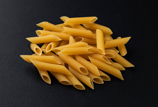 Raw penne rigate pasta isolated on black background