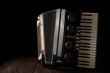 Old accordion on rustic wooden surface with black background and Low key lighting, selective focus. - obrazy, fototapety, plakaty