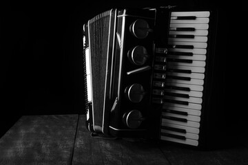 Old accordion on rustic wooden surface with black background and Low key lighting, selective focus.