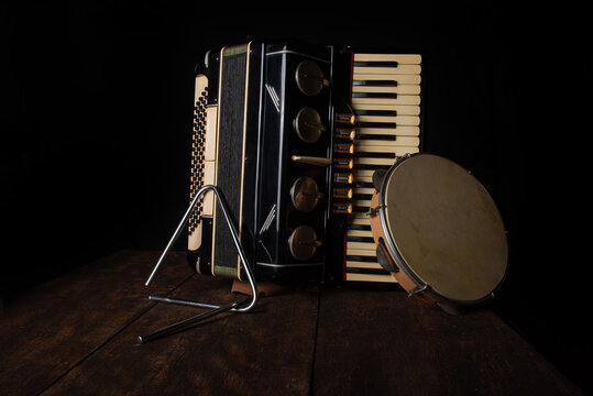 Old accordion, tambourine and triangle on rustic wooden surface with black background and Low key lighting, selective focus.
