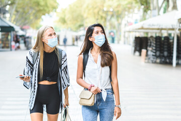 two young female tourists walking in the streets of Barcelona wearing blue protective masks