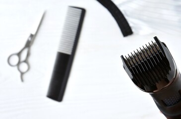 Clipper and blurred hairdressing scissors and comb on background. Hairdresser tools with selective focus on neutral background. 