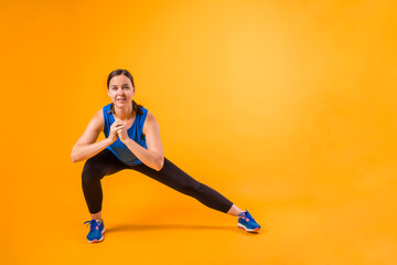 a young woman in a sports uniform performs leg exercises on an orange background