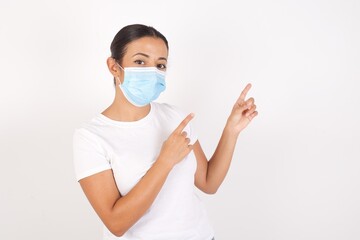 Young arab woman wearing medical mask standing over isolated white background indicating with forefinger empty space showing best low prices