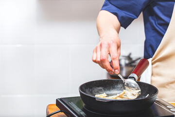 A male chef in an apron fries mushrooms champignons in a black cast-iron pan. Kitchen, food preparation, cooking.