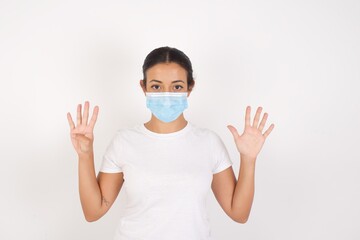 Young arab woman wearing medical mask standing over isolated white background showing and pointing up with fingers number nine while smiling confident and happy.