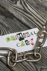 Fototapeta premium The phrase Criminal case made of letters cut from a magazine and pasted on a sheet of paper. There is a metal chain nearby. On brushed pine boards painted black and white.