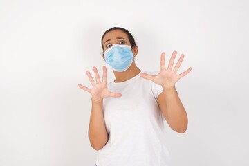 Young arab woman wearing medical mask standing over isolated white background afraid and terrified with fear expression stop gesture with hands, shouting in shock. Panic concept.