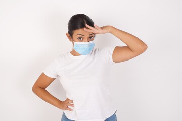 Young arab woman wearing medical mask standing over isolated white background, having problems, worried and stressed holds hand on forehead.