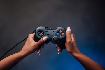 Groomed and pretty afro woman's hand is holding a joystick and pointing it up in foggy gray background. Feminine gaming.
