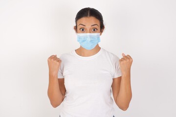 Young arab woman wearing medical mask standing over isolated white background celebrating surprised and amazed for success with arms raised and open eyes. Winner concept.