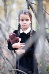 Beautiful little girl with long brunette hair, dressed in black velvet dress walks in fall forest with handmade bear toy. Halloween horror,  ghost or spirit of child in twilight