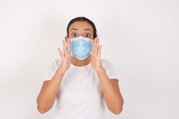 Young arab woman wearing medical mask standing over isolated white background, shouting excited to front.