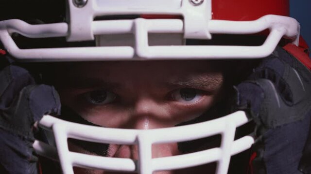 Close up portrait of determined professional American football player in helmet in bright stadium illumination lights ready for game. Confident man in uniform. Usa team game and extreme sport concept.
