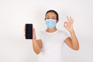 Portrait  Young arab woman wearing medical mask standing over isolated white background holding in...