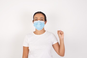 Young arab woman wearing medical mask standing over isolated white background pointing up with fingers number ten in Chinese sign language Shi