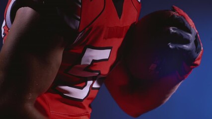 Faceless determined professional American football player in helmet holding a ball in hands. Confident man in red and white uniform. Usa game and extreme sport spirit concept.
