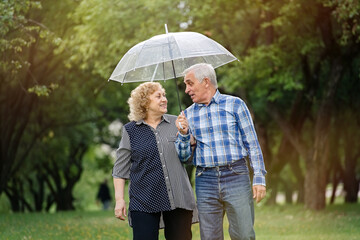 Happy senior couple walking in park during rain under umbrella