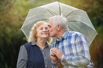 Happy senior couple walking in park during rain under umbrella