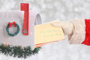 Santa Claus taking a bunch of Christmas letters coming out of a mail box with silver bokeh background and snow effect.