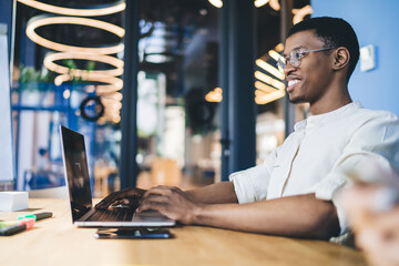 Cheerful ethnic man using laptop while sitting at table